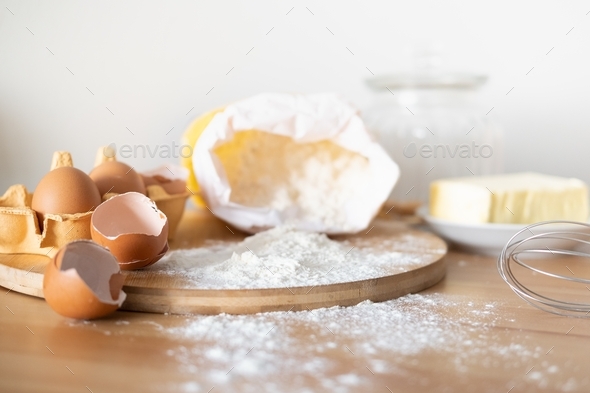 Baking cake or cupcakes ingredients - butter, flour, whisk, eggs and eggshells on wooden chalkboard
