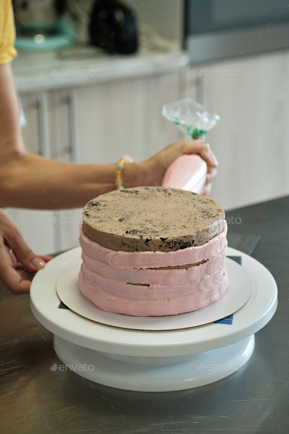 Woman spreads pink cream on cake with pastry bag, close-up. Cake making process, Selective focus