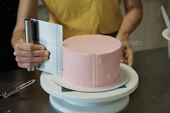 Woman spreads pink cream on cake, close-up. Cake making process, Selective focus