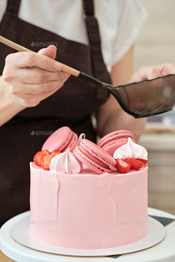Woman pastry chef decorates pink cake with macaroons and berries, close-up. Cake making process