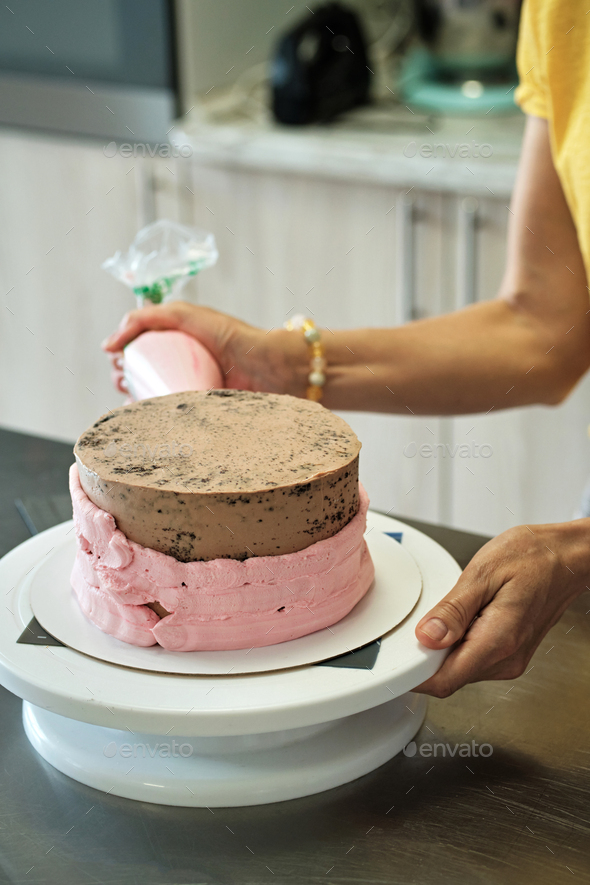 Woman making chocolate cake with pink cream, close-up. Cake making process, Selective focus