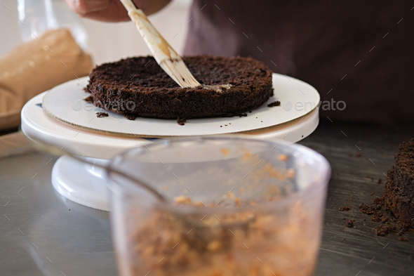 Woman pastry chef impregnates chocolate sponge cake on stand, close-up. Cake making process
