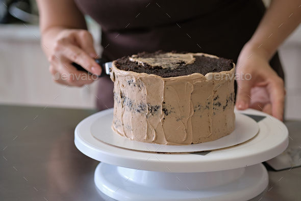 Woman pastry chef making chocolate cake with chocolate cream, close-up. Cake making process