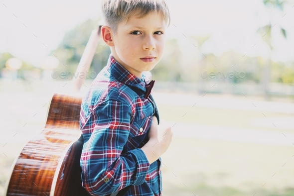 Boy in shirt with guitar in park Music lesson