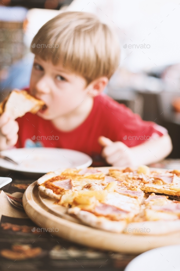 Boy bringing pizza slice up to his mouth to eat. Kids being kids Defocused face. Background