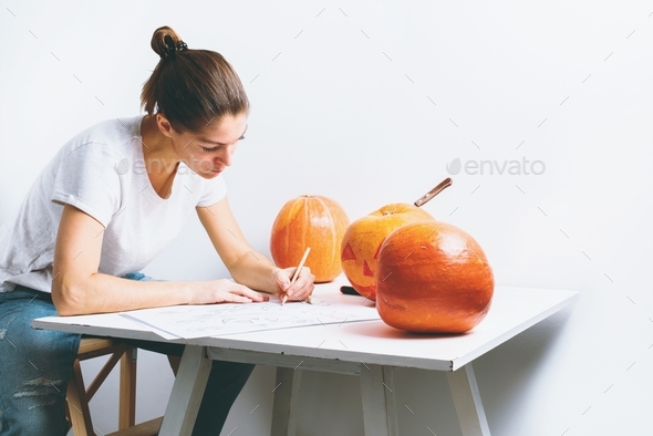 woman drawing pencil sketches character on pumpkin head preparation to halloween holiday table white