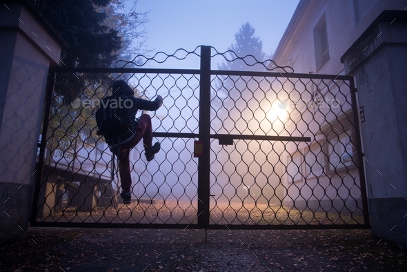 Man climbing over a fence in the night fog.