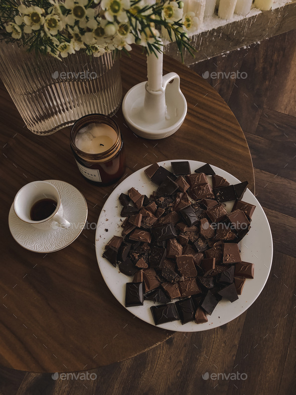 Plate of chocolate, cup of coffee, candles, flowers on wooden table. Still life. Aesthetic