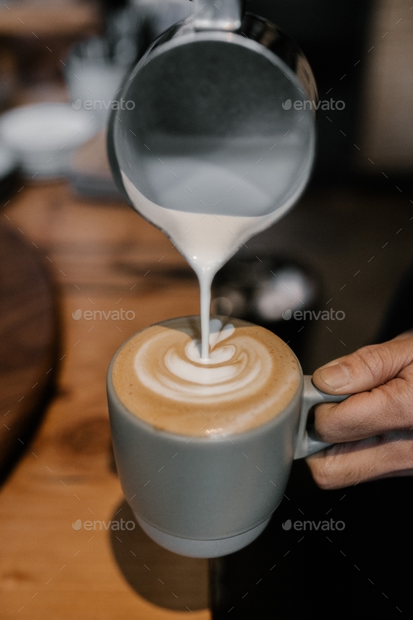 Barista pouring frothed milk into espresso to make a latte Stock Photo