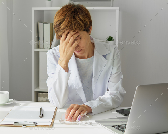 Female healthcare worker having headache. Tired and stressed doctor. Downsides of hardworking