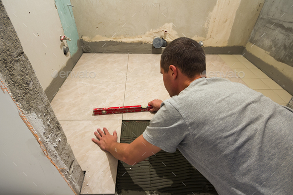 Home tiles improvement - handyman with level laying down tile floor.