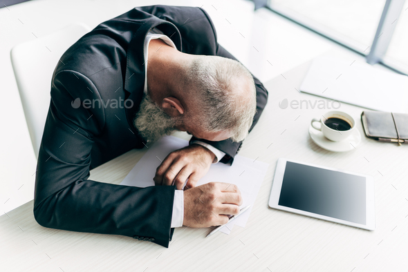 top view of overworked senior businessman sleeping at workplace with office supplies