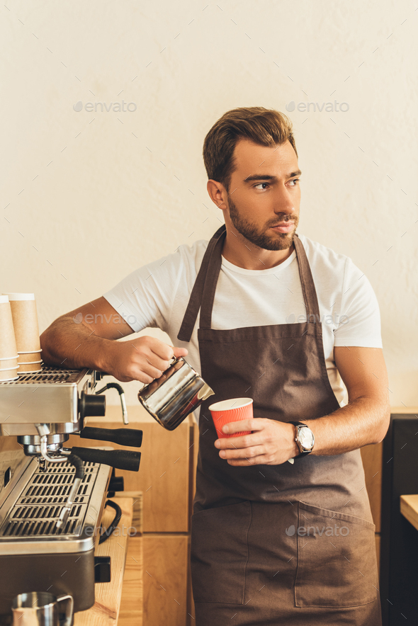 portrait of barista pouring milk into paper cup while making coffee to ...