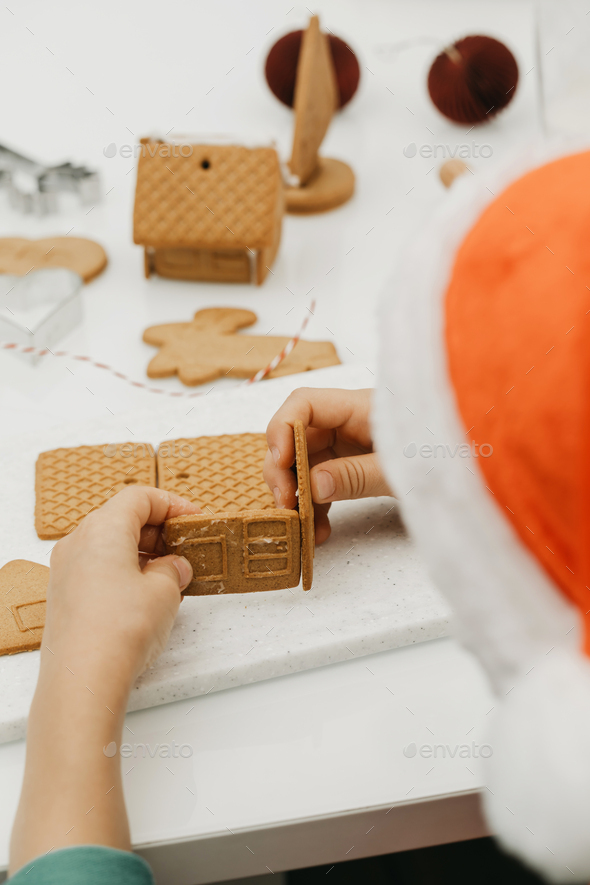 A Child In A Santa Hat Makes A Gingerbread Gingerbread House. New Year 