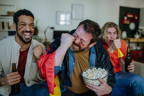 Happy German football fans friends watching football at home and eating popcorn.