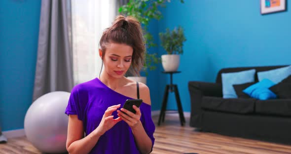 A Pretty Young Woman Dressed in Fitness Clothes Sits on the Wooden Floor of an alt