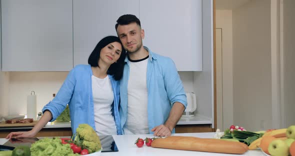 Smiling Married Couple in Love Standing on Kitchen Background and Posing on Camera alt