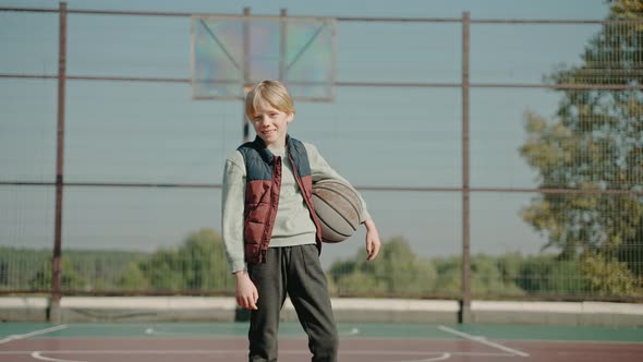 Boy Stands on a Court Holding Basketball Ball and Looking at the Camera