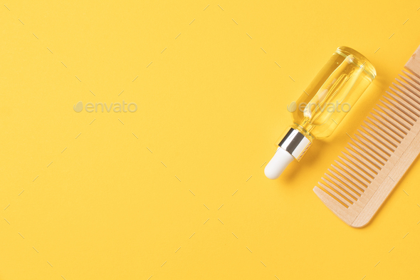 Natural hair care oil and wooden comb on yellow background, top view. copy space