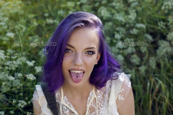 portrait teenager girl with purple hair shows his tongue with a piercing