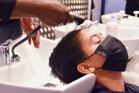 mixed race young woman getting hair washed at hair dresser, with face mask on