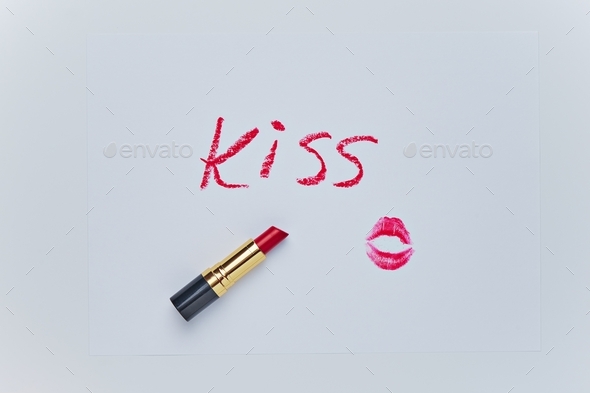 Text KISS drawing and trace of kiss by red lipstick on white sheet. Sketch closeup on white backdrop