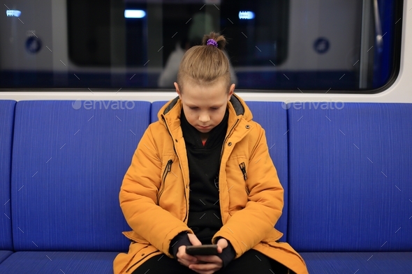 A boy in a yellow jacket is alone in public transport. teenager on the subway playing in phone