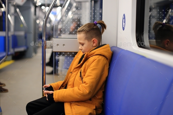 A boy in a yellow jacket is alone in public transport. teenager on the subway in mobile phone