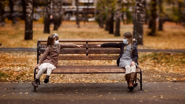 children sit on a bench wearing masks, social distance and friendship