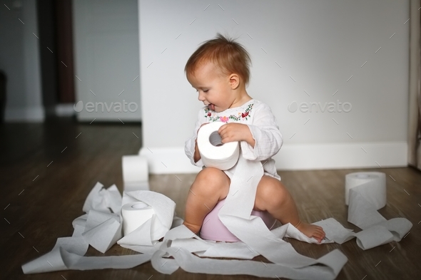 Cute child Toddler sits on pot with a lot of rolls toilet paper, hygiene and sanitary
