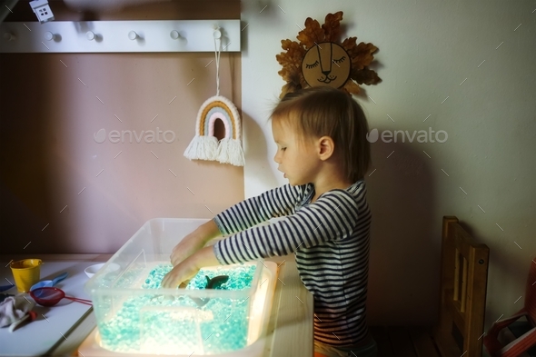 Child plays in the light sensor box with hydrogel, children\'s hands play with blue water beads