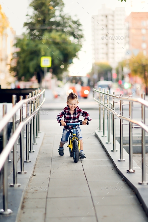 Stylish cute european boy on balance bike in the city, child rides a ...