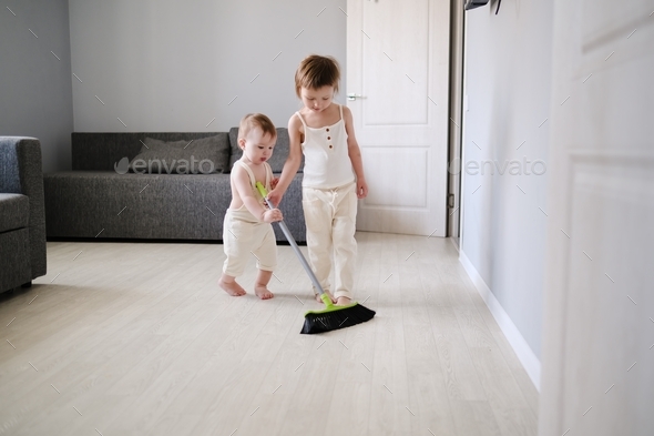 Children siblings with mop sweep floor in bright living room, help with housework