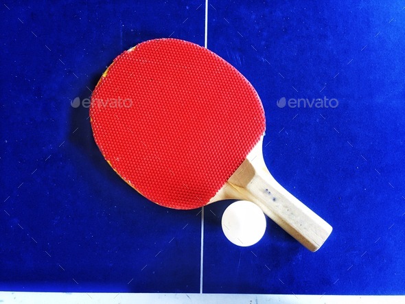 Red table tennis bat and ball on blue ping pong table in a leisure sports background with copy space
