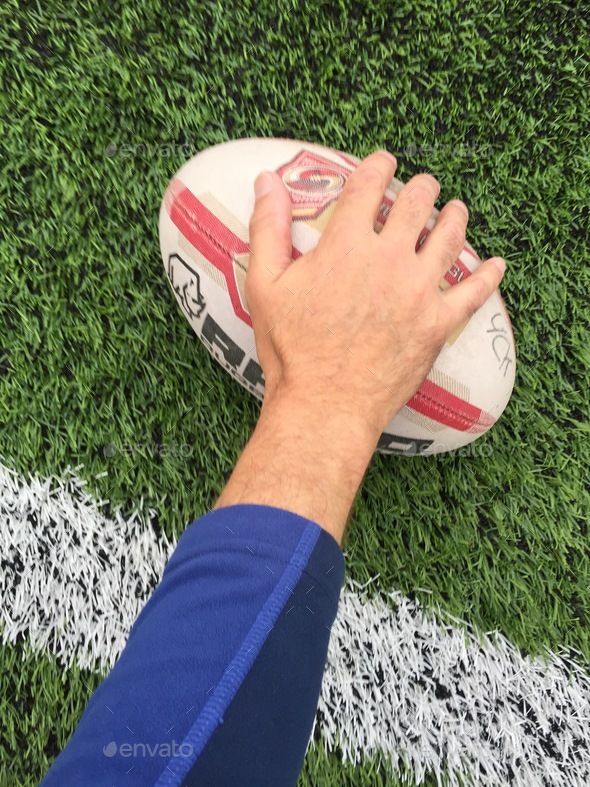 A rugby player’s hand and arm reaching over the try line to touch the ball down for a score on grass