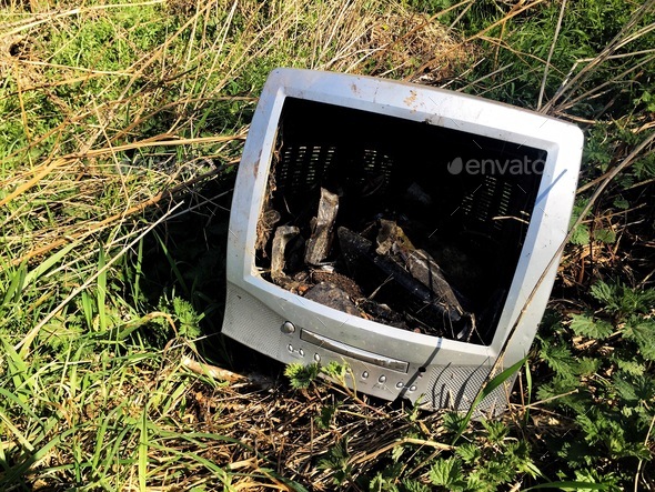 An old computer monitor or TV that has been dumped on a scrapheap fly tipping on wasteland