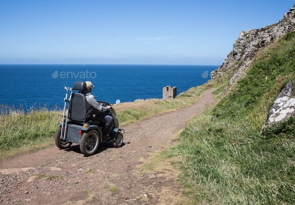 Senior man riding a mobility scooter or tramper over rough terrain in an independence concept image