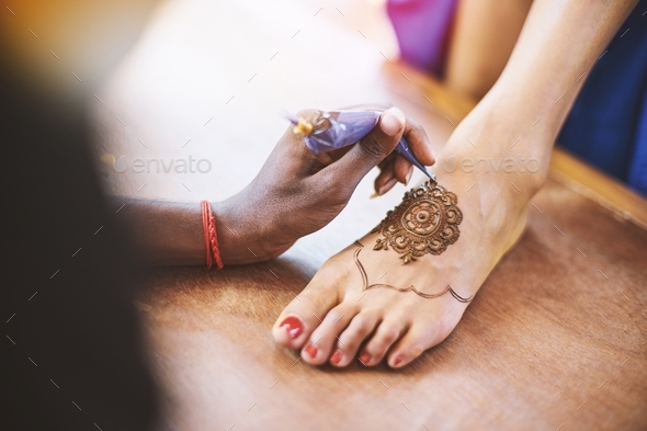 The Indian henna artist drawing the tattoo art (Mehndi) on the women foot on the indian wedding day