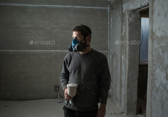 a young man is standing in a construction respirator on his face and with a spray gun