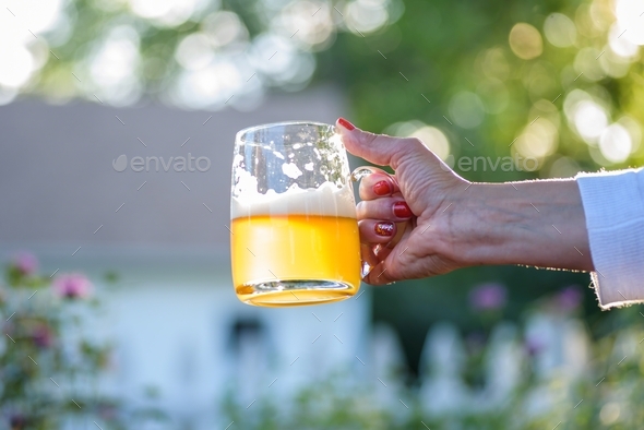 Woman holding a large glass mug of beer outside in sunlight