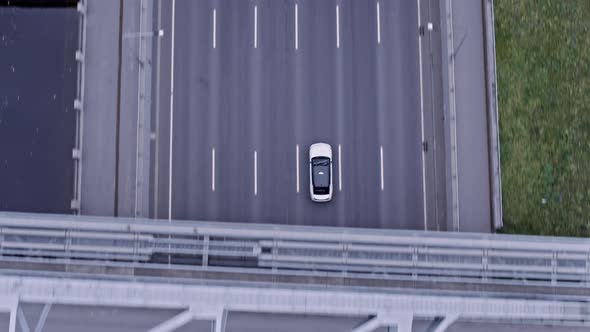 Drone footage of white car drives under the American bridge.