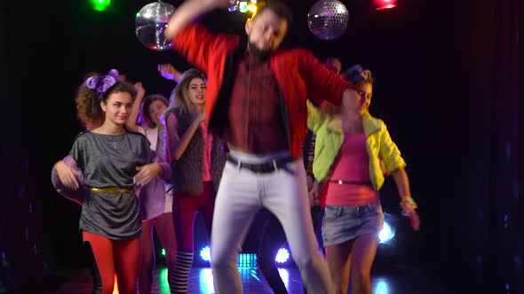 Guy Stands in Sadness Around a Crowd of Cheerful People Dancing. Black Background alt