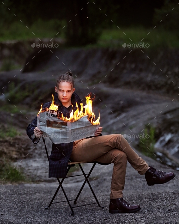 young guy holding a burning newspaper in his hands