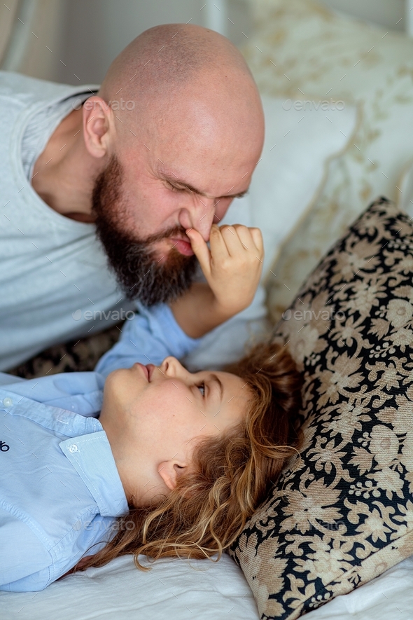 dad and son are playing on the bed, the boy grabbed dad by the nose