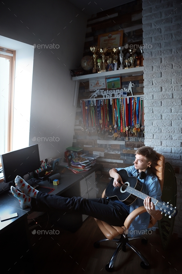 college student in his youth room. The guy plays the guitar around the awards and the computer