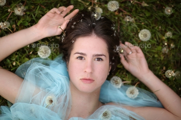Portrait Of A Dark Haired Girl Lying On The Grass Among Dandelions