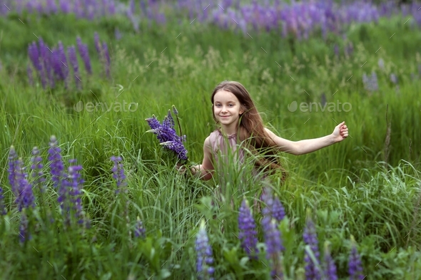 a little lion about eight years old runs through a field of lupins with a flower in her hand