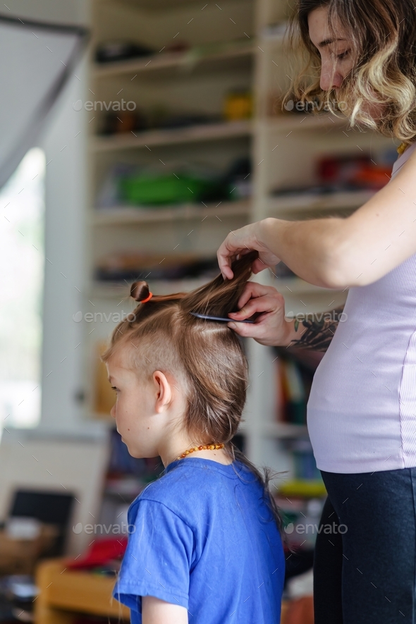 Pregnant mother cutting her son’s hair at home Stock Photo by souslesoleil
