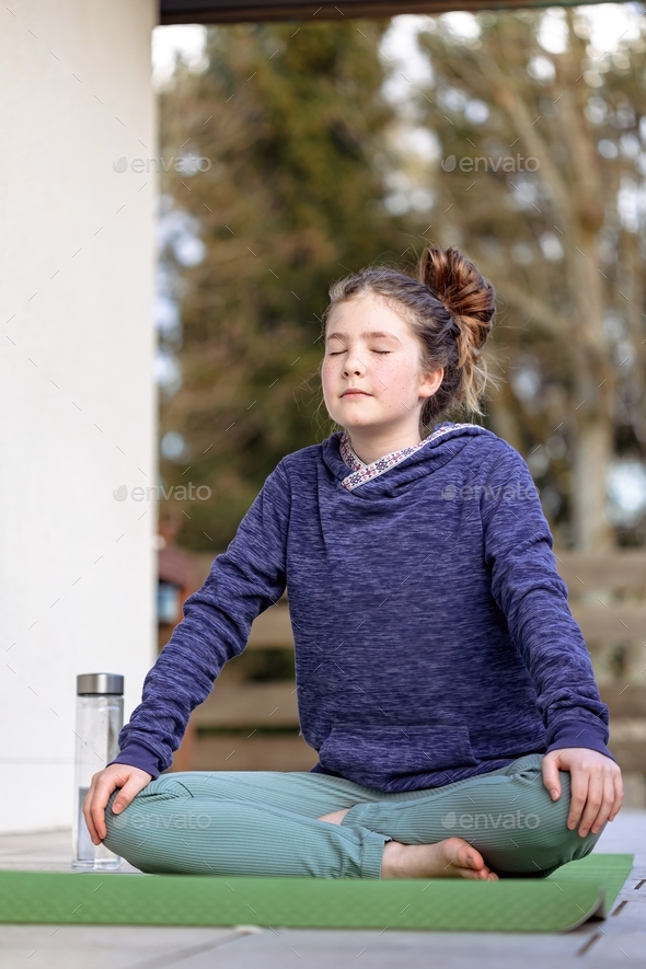 The girl is doing yoga, sitting on a mat on the veranda of the house on