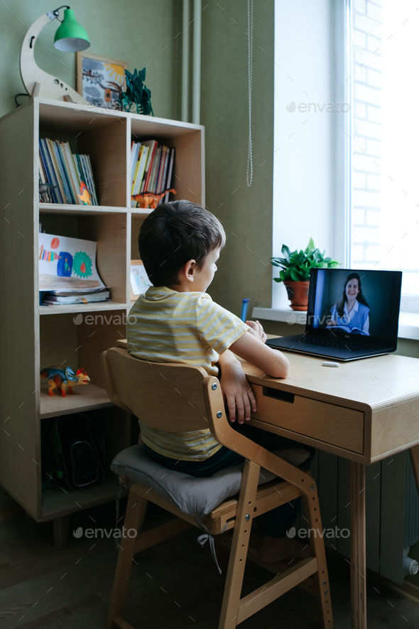 8 years old boy sit by desk with laptop and do writing task during